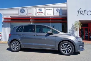 Vue de profil côté gauche d'une Volkswagen Golf Sportsvan gris Indium Metal stationnée devant un garage multimarques.