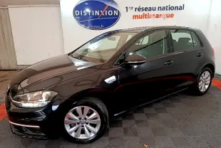 Volkswagen Golf noire vue de 3/4 avant droit, avec jantes alliage et phares halogènes visibles en intérieur showroom.