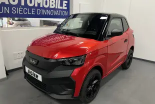 Vue 3/4 avant droite d'une LIGIER JS50 BEV 8KWH ELITE rouge avec toit noir et jantes alu noires en intérieur showroom.