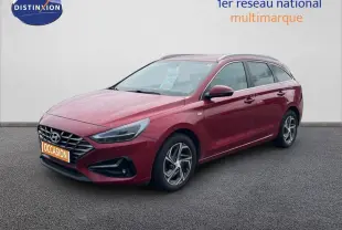 Vue 3/4 avant droite d'une Hyundai i30 SW 2023 rouge Sunset Red Metal avec jantes alliage et calandre distinctive.