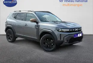 Dacia Duster gris 3/4 avant droit avec jantes noires et rétroviseurs couleur bronze sur fond clair.