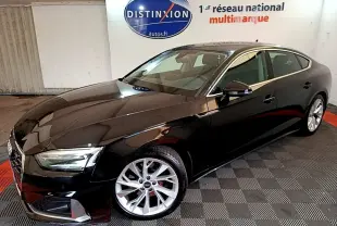 Audi A5 noir vue 3/4 avant droit dans un showroom avec jantes argentées et phares LED allumés.