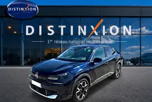 Citroën C4 X bleu en 3/4 avant droit, avec jantes alu et calandre distinctive, devant une vitrine Distinxion.