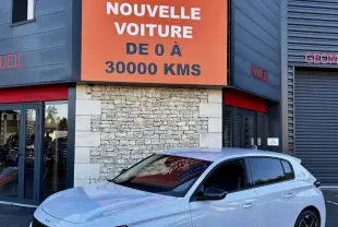 PEUGEOT 308 Hybrid blanc vue 3/4 avant droit, calandre noire et feux LED verticaux, devant un bâtiment commercial.