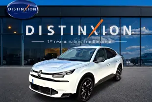 Vue 3/4 avant d'une Citroën C4 X blanche avec jantes noires, devant une vitrine Distinxion.