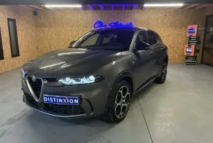 Alfa Romeo Tonale gris foncé vue 3/4 avant droit, phares allumés et jantes distinctives en intérieur showroom.