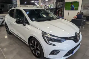 Renault Clio V TCe 100 GPL blanc glacier vue 3/4 avant droit en intérieur avec jantes noires bicolores.