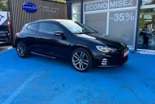 Volkswagen Scirocco noir intense vue 3/4 avant droit sur parking bleu devant vitrine avec promotion -35%.