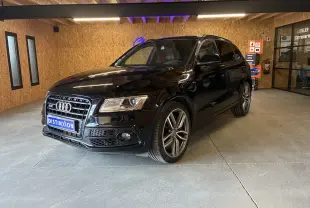 Audi SQ5 noir vue 3/4 avant droit, avec jantes alu et calandre distinctive dans un intérieur bois clair.