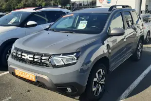 Dacia Duster gris 2024 en 3/4 avant droit, avec jantes bi-ton et plaques "Occasion" visible au parking.