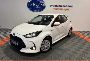 Toyota Yaris hybride blanche vue 3/4 avant droit en intérieur avec phares et antibrouillard allumés.