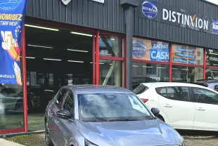 Peugeot 208 110 hybrid gris vue 3/4 avant droit, avec calandre noire et feux LED distinctifs, devant un garage.