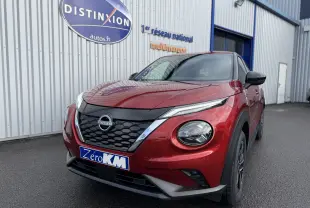 Nissan Juke 1.6 Hybrid rouge Fuji en 3/4 avant droit, avec calandre noire et phares ronds distinctifs.