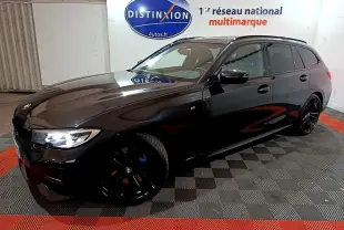 BMW Série 3 318i M Sport noire vue en 3/4 avant droit avec jantes noires et phares allumés dans un showroom
