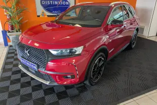 Vue 3/4 avant d’un DS7 rouge 2019 avec attelage, jantes noires et calandre distinctive dans un showroom.