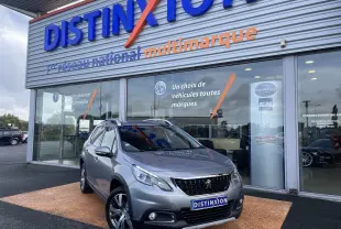 Peugeot 2008 gris en 3/4 avant droit devant une concession Distinxion, avec jantes alliage et calandre noire.