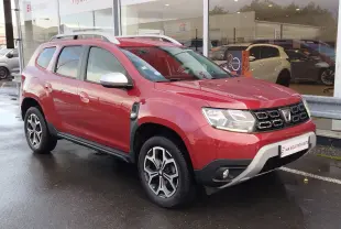 Vue 3/4 avant droit d'un Dacia Duster rouge Fusion 2020 avec jantes alliage bicolores et barres de toit argentées.