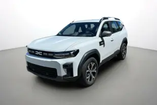 Dacia Bigster blanc glacier en 3/4 avant droit, avec barres de toit et jantes alu 17 pouces visibles.