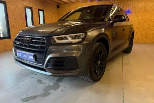 Audi Q5 Sportback gris en vue 3/4 avant droit, avec jantes noires et calandre imposante dans un intérieur en bois.