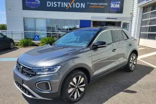 Volkswagen T-Roc gris Indium en 3/4 avant droit, avec attelage amovible visible, stationné devant un concessionnaire.