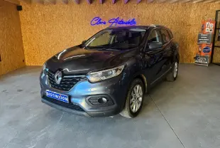 Renault Kadjar gris 2019 en 3/4 avant droit dans un garage avec mur en bois et enseigne lumineuse bleue.