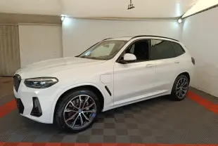 BMW X3 xDrive30e blanc en 3/4 avant droit, avec jantes alliage et prises de recharge latérales visibles.