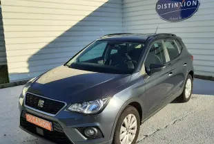 SEAT Arona gris magnetic avec toit noir, vue 3/4 avant droit, garée devant un mur blanc avec panneau Distinxion.