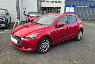 Vue 3/4 avant d'une Mazda2 rouge brillante avec jantes aluminium, stationnée devant un concessionnaire.