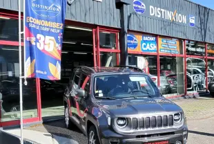 Jeep Renegade Granite Crystal métallisé en 3/4 avant droit, stationnée devant un garage avec enseignes commerciales.