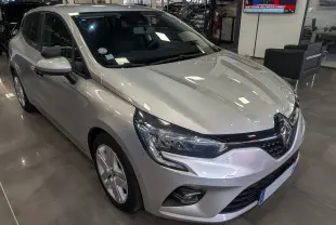 Renault Clio V gris platine vue 3/4 avant droit en showroom, avec phares LED et calandre noire brillante.