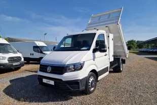 Volkswagen Crafter blanc vu 3/4 avant droit avec benne relevée et coffre latéral sur terrain gravillonné.